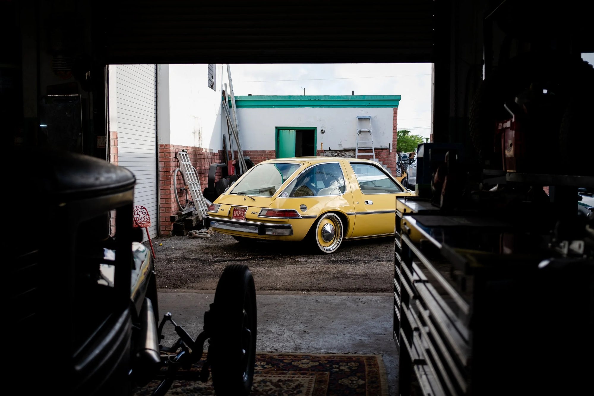 Yellow AMC Pacer classic car parked outside a garage with a toolbox in the foreground.
